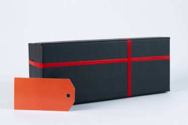 Kırmızı kurdeleli siyah hediye kutusu ve beyaz arka planda izole edilmiş etiket.