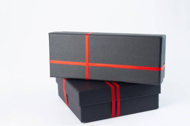 Beyaz arkaplanda kırmızı kurdeleli siyah hediye kutusu.