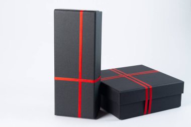 Beyaz arkaplanda kırmızı kurdeleli siyah hediye kutusu.