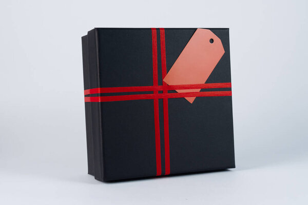 Black gift box with red ribbon and tag isolated on white background.