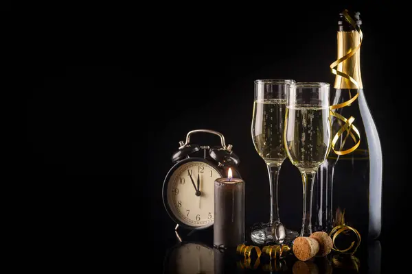 Champagne flutes and alarm clock on black background with copy space, New Year and Christmas celebration concept.