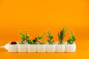  Turuncu arka plandaki beyaz plastik soketteki bitkiler. Boşluğu kopyala.