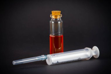 Siyah zemin üzerinde renkli sıvı ve şırınga bulunan tıbbi ampuller