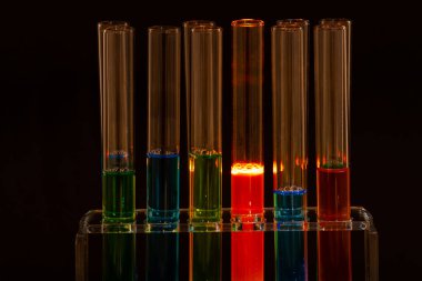 Siyah arka planda renkli sıvılar bulunan laboratuvar test tüpleri.