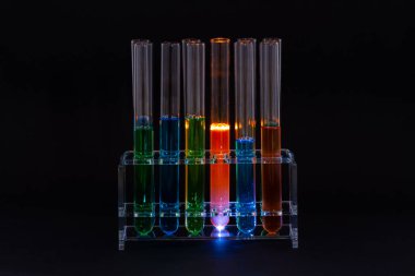 Siyah arka planda renkli sıvılar bulunan laboratuvar test tüpleri.