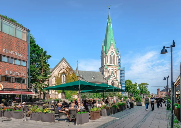 Kristiansand, Norveç - 15 Ağustos 2022: İnsanlar arka planda Katedral ile şehir merkezinde güneşli bir günün tadını çıkarıyor.