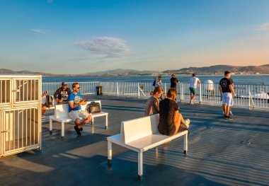 Saronic Körfezi, Yunanistan - 22 Haziran 2023: Bir feribotun güvertesindeki insanlar güneşin doğuşunun keyfini çıkarıyorlar. Gemi az önce Pire Limanı 'ndan ayrıldı ve yolcuları Cyclades Adaları' na taşıdı..