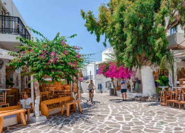 Antiparos, Yunanistan - 23 Haziran 2023: Beyazlatılmış evler, bougainvillea ağacı ve kaldırım kafeleri olan geleneksel kaldırım taşı sokağı.