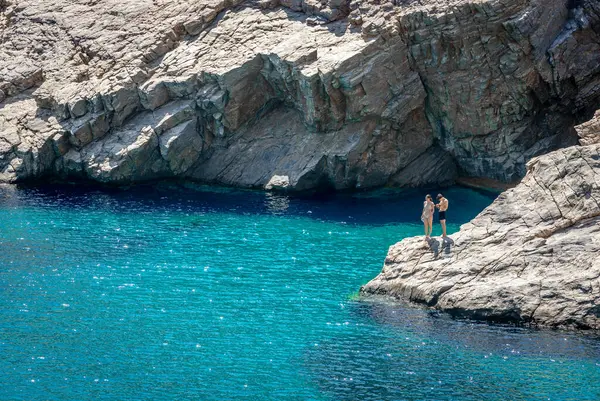 Yunanistan 'ın Amorgos kentindeki Mouros plajı - 25 Temmuz 2024: Sahilin sonundaki kayalıklarda genç bir çift duruyor. Mouros plajı Amorgos, Cyclades, Yunanistan 'da inanılmaz bir çakıl taşı plajı..
