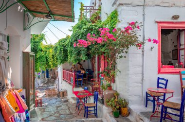 Yunanistan 'ın Amorgos kentinden Chora - 27 Temmuz 2024: Ege Adası' nın başkentinde beyazlatılmış evler ve açık kafeler bulunan dar kaldırım taşı caddesi.