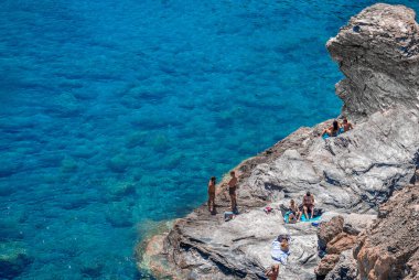 Yunanistan 'ın Amorgos kentindeki Mouros plajı - 25 Temmuz 2024: Yüzücüler denizde ve plajın uzak ucundaki kayalıklarda. Mouros plajı Amorgos, Cyclades, Yunanistan 'da inanılmaz bir çakıl taşı plajı..