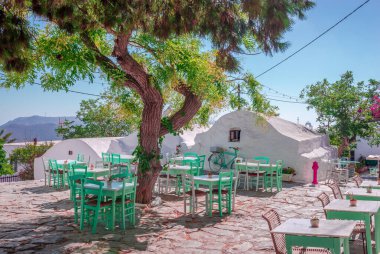 Yunanistan 'ın Cyclades kentindeki Amorgos Adası' nın başkenti Hora meydanındaki açık kafe. Ağacın gölgesinde beyazlatılmış evler ve masalar.