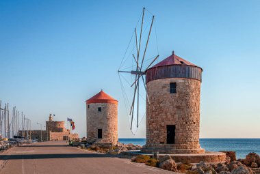 Mandraki limanındaki uzun dalga kırıcının üzerinde yer alan Rodos, Yunanistan 'da bu ortaçağ yel değirmenleri ayakta duruyor. Arka planda Agios Nikolaos (Aziz Nicholas) kalesi ve deniz feneri yer almaktadır..