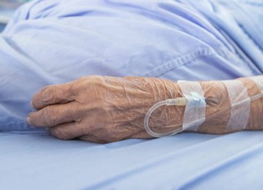 Hastane koğuşunda yatarken damardan sıvı enjekte etmek için yaşlı bir hastanın elini kapat. 