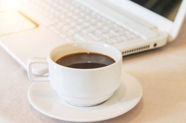 Sıcak kahveyi, beyaz dizüstü bilgisayarlı beyaz bardakla kapatın. 