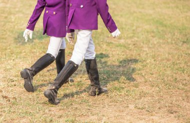 Young girl equestrians in professional apparel  dressage purple jacket competition with black leather horseman boots walking in the field clipart