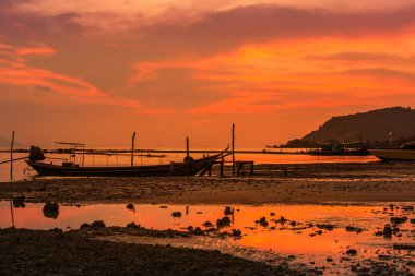                    Gün batımında tropikal sahilde yüzen balıkçı teknesi olan siluet balıkçıları.