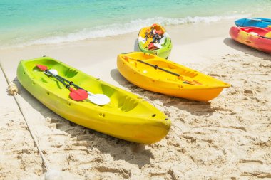 Güneşli bir günde turkuaz denizle kıyıya demirlemiş renkli sarı kanolar, tatil için gidilecek yer.