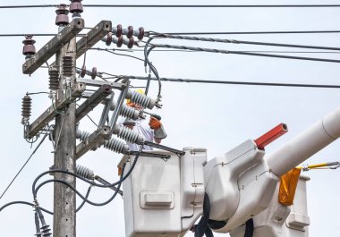 Elektrik tesisatçısı elektrik direğindeki elektrik hattının kablosunu tamir ederken hidrolik kaldırma platformunda çalışıyor.
