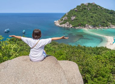 Yükseklerdeki kayalıklarda oturan ve el kaldıran kadın kollarını açmış kutlama yapıyor Koh Nang Yuan Adası, Surat Thani, Tayland 'daki tepenin zirvesine çıktıktan sonra manzaranın tadını çıkarıyor.