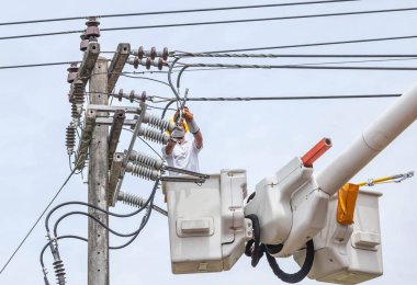 Elektrik tesisatçısı elektrik direğindeki elektrik hattının kablosunu tamir ederken hidrolik kaldırma platformunda çalışıyor.