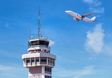 Uluslararası havaalanında hava trafik kontrol kulesi ve mavi gökyüzünde uçan bir uçak.
