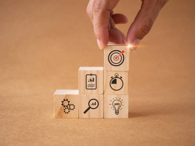 İkonların hedefiyle el ele tutuşan tahta küpler, kahverengi iş arka planında iş stratejisi. Eylem planı, hedeflere ulaşmayı planlama, iş geliştirme konsepti. Boşluğu kopyala