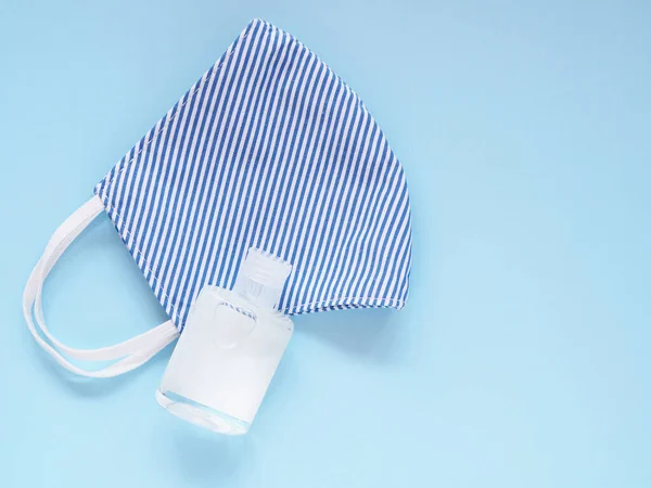 Top view, Fabric face mask blue-white stripes and alcohol gel in bottle to prevention pollution and viruses. DIY handmade from cotton muslin on blue background. Healthcare, Medical and New normal concept. Copy space for your text