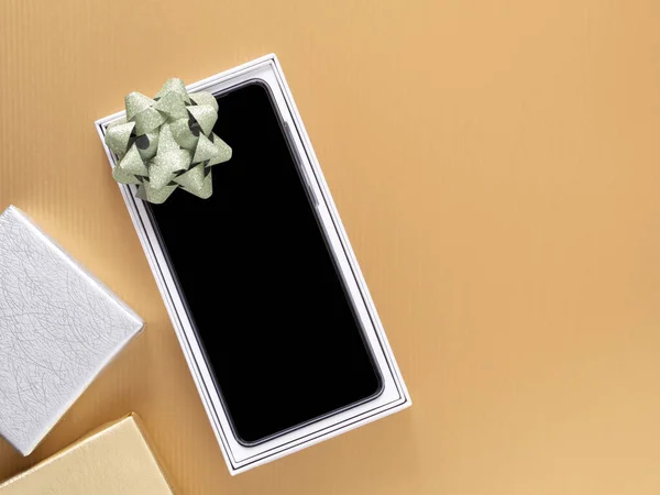 Stock image Festival gift-giving concept, Top view, New smartphone in box with a green bow on gold paper background.