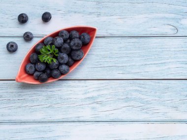 Üst manzara, mavi ahşap arka planda yapraklı kırmızı plakalı taze yaban mersini. Fotokopi alanı olan düz bir yer. Sağlıklı yeme ve beslenme kavramı, Superfood