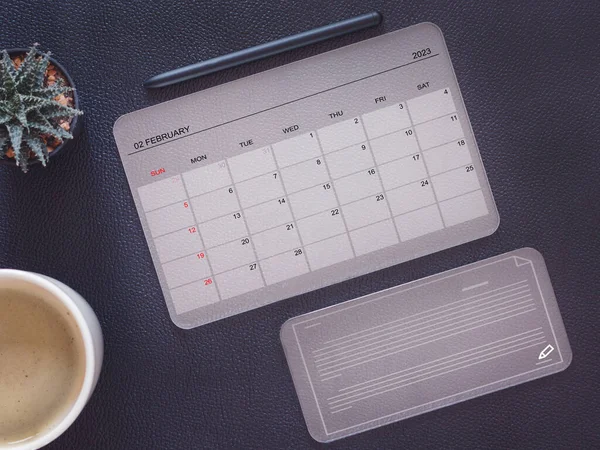 Top view, transparent tablet pc computer showing February 2023 calendar page, with transparent smartphone and cactus, coffee cup. Business concept and education. Calendar app with planning