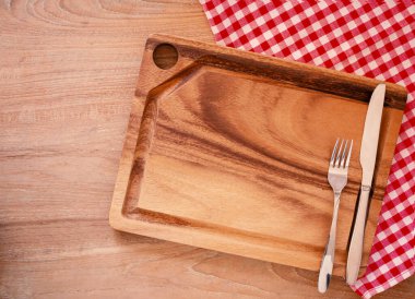 Mavi ve beyaz kareli kumaş, peçete ve bıçak üzerinde boş kesim tahtası, kırsal ahşap arka planda çatal. Mutfak gereçleri ve sofra takımları hariç. Gıda ürünleri için maket yapın. Üst görünüm, kopyalama alanı olan düz uzanma. 