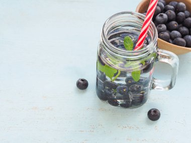 Taze organik yaban mersinli su ve mavi ahşap arka planda saman içmek. Metnin için boşluk.