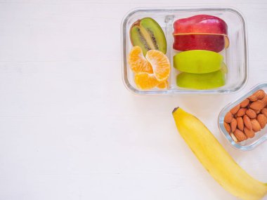 Elmalı, kivili, muzlu, portakallı, beyaz ahşap arka planda bademli taze meyve. Yemeği götür. Fotokopi alanı, sağlıklı beslenme kavramları