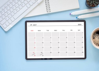 Tablet bilgisayarındaki çevrimiçi takvim uygulaması Temmuz 2023 'ü gösteriyor mavi arkaplan, klavye, defter, kaktüs. Zamanlama planlama için takvim uygulaması ile anımsatıcı. Üst görünüm