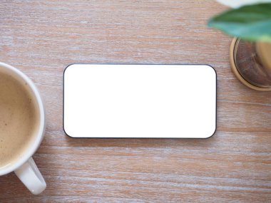 Üst manzara, boş beyaz ekranlı akıllı telefon ve küçük ağaç, ahşap arka planda kahve. Şablon, ürünün metin ve logosu için cep telefonu boş ekran maketi. 