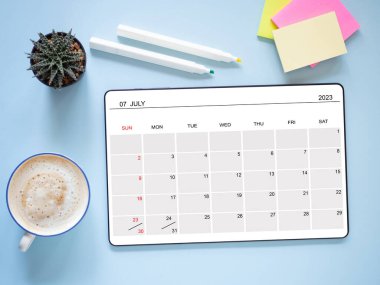 Tablet bilgisayarındaki çevrimiçi takvim uygulaması Temmuz 2023 'ü gösteriyor, mavi arka plan, kahve fincanı, kaktüs ve post-it notu. Üst manzara, düz yatış. Zamanlama planlaması için anımsatıcı.