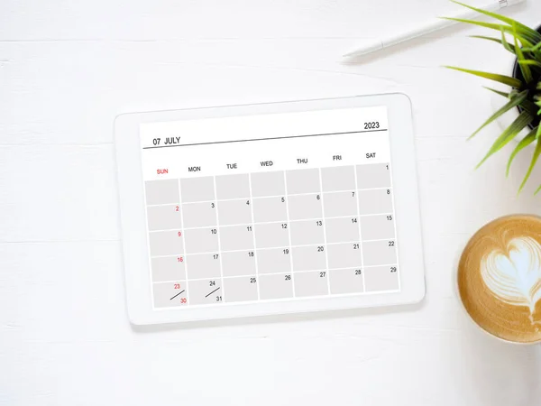 stock image Tablet computer with an open app of the calendar for July 2023 year and a cup of coffee on white background for setting weekly, and monthly goals to achieve the goals set. Concept schedule plannin