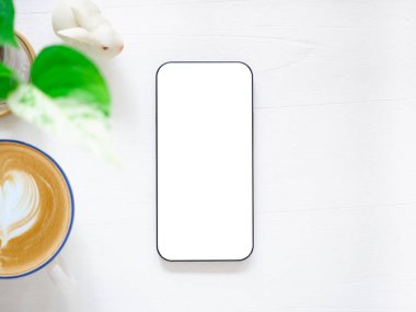 Üst manzara, beyaz beyaz ekranlı akıllı telefon ve kahve fincanı, bitkiler, beyaz ahşap arka plandaki tavşan heykeli. Şablon, ürünün metin ve logosu için cep telefonu boş ekran maketi