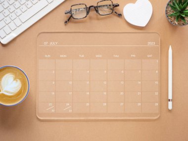 Üst görünüm, saydam tablet bilgisayar Temmuz 2023 takvim uygulama sayfası ve kaktüs, kahve fincanı, kalem, klavye kahverengi arka planda. Zamanlama planlaması için takvim uygulaması