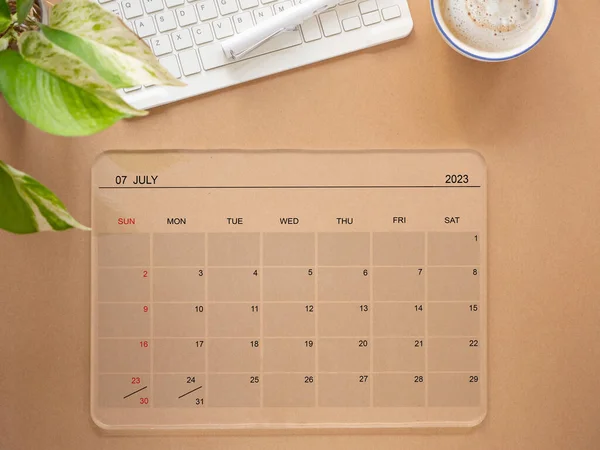 Online calendar app on transparent tablet computer showing screen July 2023, on brow table and keyboard for setting weekly, and monthly goals to achieve the goals set. Reminder for schedule plannin
