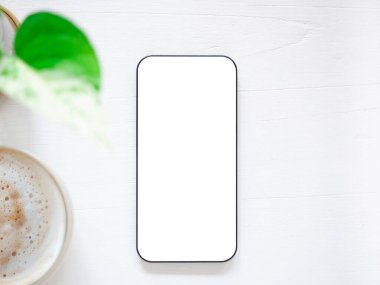 Üst manzara, beyaz beyaz ekranlı akıllı telefon ve kahve fincanı, beyaz ahşap arka planda bitkiler. Şablon, ürünün metin ve logosu için cep telefonu boş ekran maketi