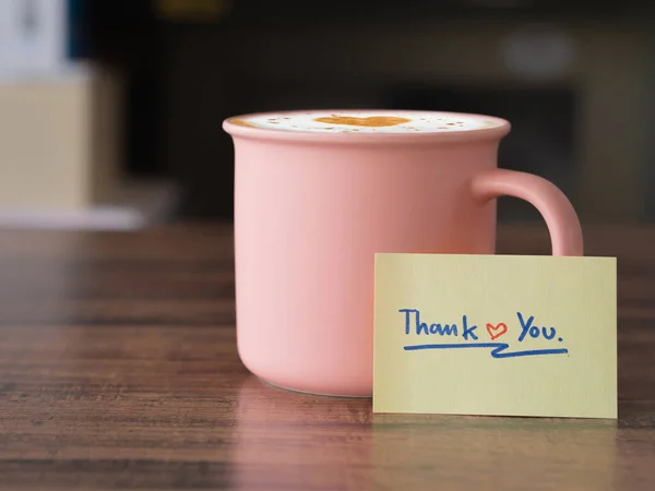 ポジティブで感謝のコンセプト 茶色の木のテーブルのピンク色の陶磁器のマグの手書きのテキスト ありがとう メッセージそして熱いラテのコーヒー — ストック写真