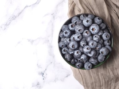 Üst manzara, organik olgun yabanmersinlerinin seramik kasede olduğu düz bir yer ve mermer taştan arka planda gri bir bez. Sağlıklı yeme ve beslenme kavramı, Superfood