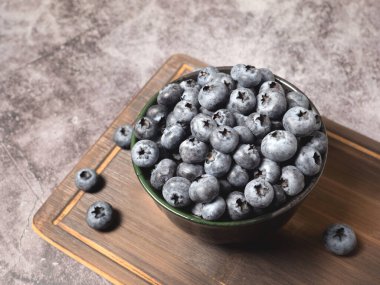 Gri arka planda kesme tahtasının üzerinde olgun taze yaban mersinleri. Sağlıklı yeme ve beslenme konsepti
