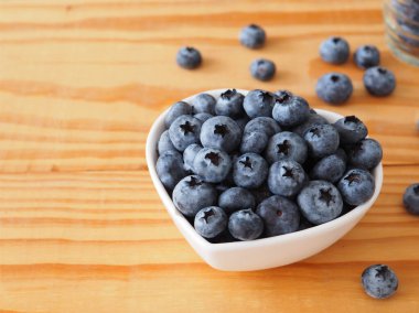 Kalp şeklinde taze yaban mersinleri ahşap arka planda beyaz kase şeklinde. Sağlıklı beslenme ve beslenme kavramı metnin için geniş bir bakış açısı. Süper yemek.