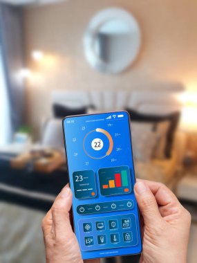 Odadaki ışık ve sıcaklığı kontrol etmek için akıllı telefonu kullanan biri. Cep telefonundaki akıllı ev otomasyon sistemi. Akıllı yaşam. Yaşam tarzı ve teknoloji. Akıllı ev teknolojisi kavramı  
