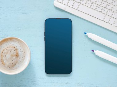 Üst manzara, fotokopi alanı olan düz bir yer. Mavi ofis masasında akıllı telefon maketi, kahve fincanı, klavye bilgisayarı. İnternet alışverişi, blog, logo, ürün ve sosyal medya kavramları