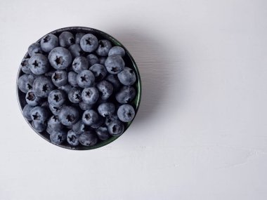 Üst manzara, bembeyaz ahşap zemin üzerine seramik kasede taze böğürtlen dolu organik olgun yaban mersinlerinin olduğu düz bir yer..