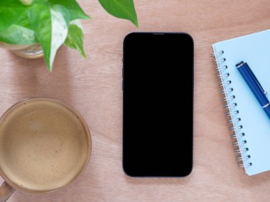 Cep telefonunun boş görüntüsü, kahve fincanı, bitki, kalem, defter ve ahşap arka planda. Üst görünüm bileşimi. Konsept alışverişi, blog, logo, ürün ve sosyal medya.  